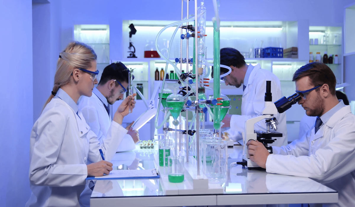 دکوراسیون آزمایشگاه حرفهای با تحویل دقیق؛ از ایده تا اجرا 6 متخصصان آزمایشگاه با پوشش ایمنی در حال کار با تجهیزات اپتیکال، سیستمهای لولهگذاری شیشهای و محلولهای شیمیایی